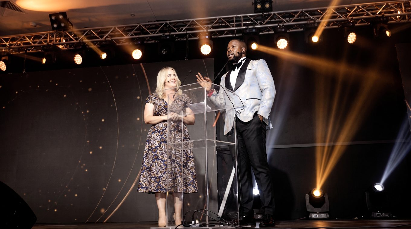 On stage with a co-host under spotlight beams